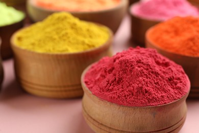 Photo of Colorful powders in wooden bowls on pink background, closeup with space for text. Holi festival celebration