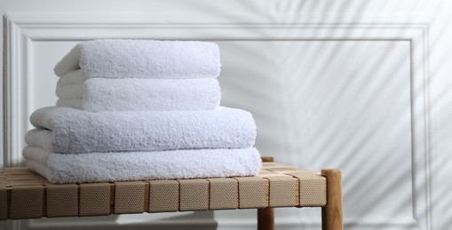 Photo of Stacked terry towels on wicker bench indoors, space for text