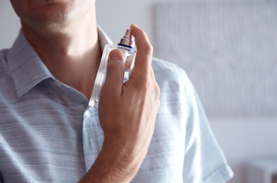 Photo of Young man with bottle of perfume indoors, closeup