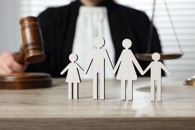 Family law. Judge with gavel sitting at wooden table, focus on figure of parents and children