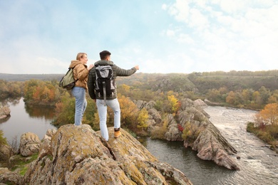 Photo of Couple of hikers with travel backpacks enjoying beautiful view near mountain river
