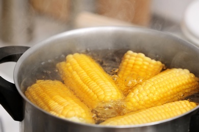 Photo of Stewpot with boiling water and corn cobs, closeup