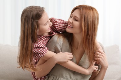 Photo of Mother with her cute daughter spending time together on sofa at home