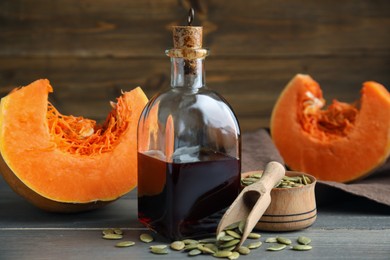 Photo of Glass bottle of oil with cut pumpkin and seeds on wooden table