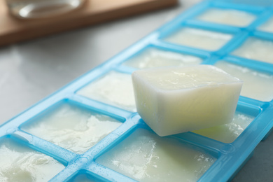 Ice cube tray with frozen milk on grey table, closeup