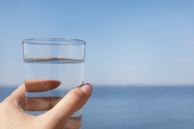 Photo of Woman holding glass of refreshing drink near sea on hot summer day, closeup. Space for text
