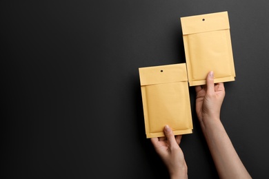 Photo of Woman holding kraft paper envelopes on black background, closeup. Space for text
