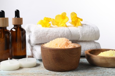 Photo of Natural sea salt in bowls and other spa supplies on wooden table against white background