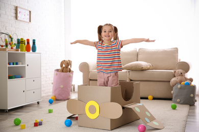 Photo of Cute little child playing with cardboard plane at home
