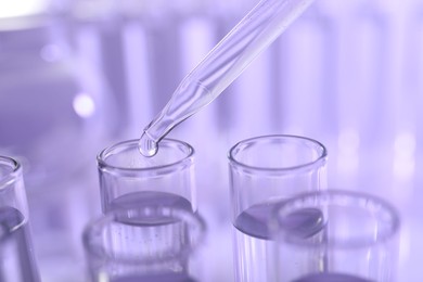 Dripping liquid from pipette into test tube on violet background, closeup