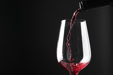 Photo of Pouring red wine into glass against black background, closeup. Space for text