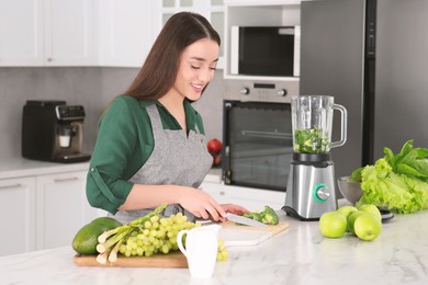 Photo of Young woman cutting broccoli for smoothie at white table in kitchen
