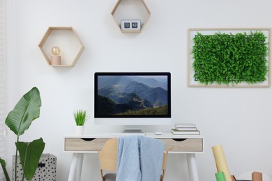 Photo of Green artificial plant wall panel and desk with computer in light room. Interior design