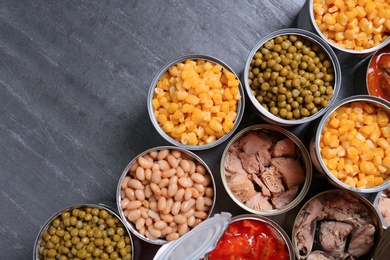 Photo of Open tin cans of conserved products on grey table, flat lay with space for text
