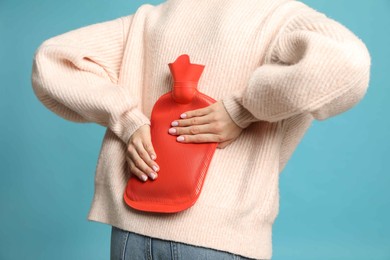 Photo of Woman using hot water bottle to relieve back pain on light blue background, closeup
