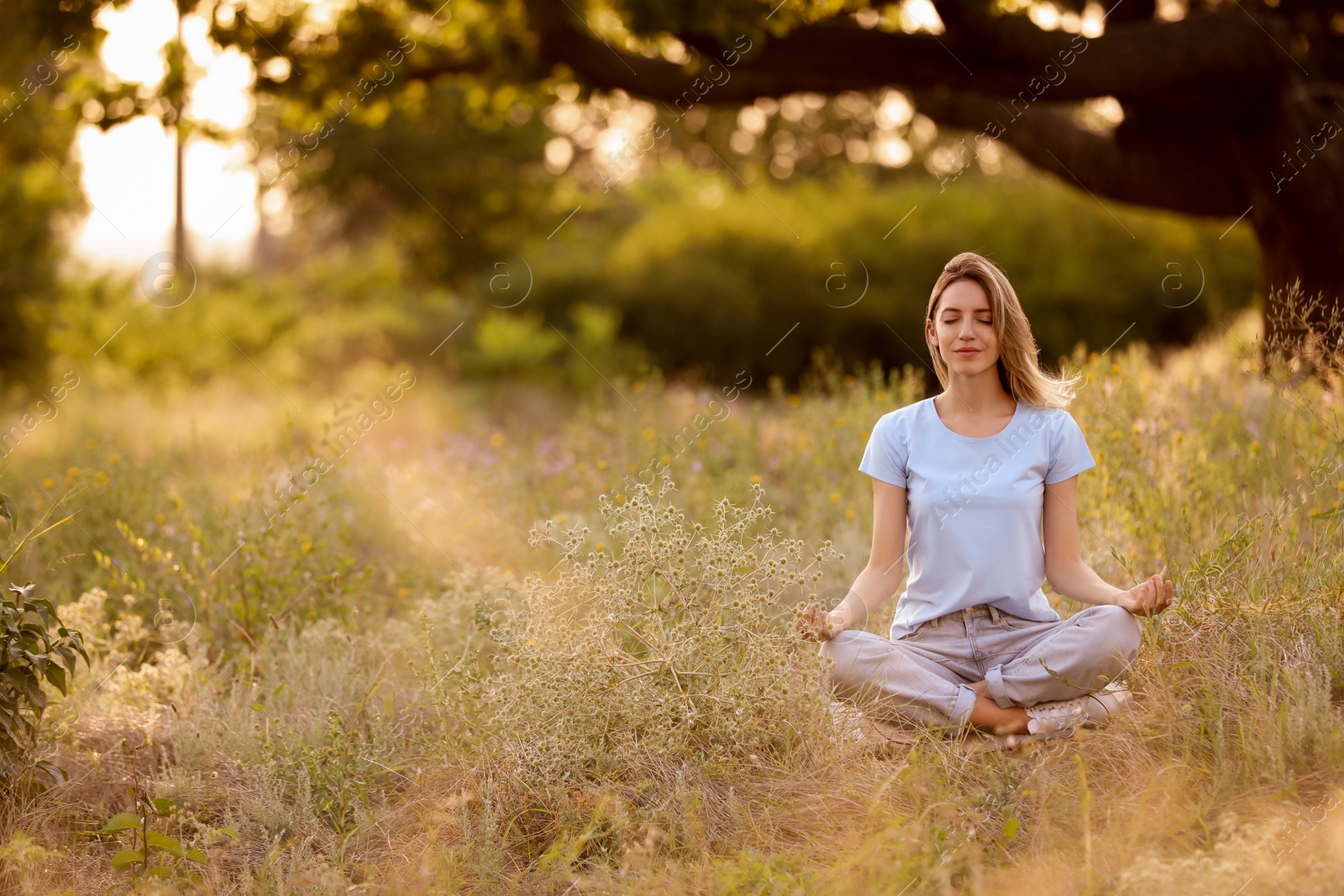 Photo of Young woman meditating on green grass in park, space for text