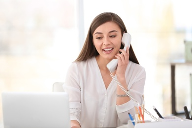 Photo of Young woman talking on phone at workplace