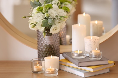 Beautiful burning candles, books and flowers on table at home