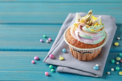 Photo of Cute sweet unicorn cupcake and festive decor on light blue wooden table, space for text