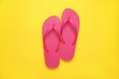 Stylish pink flip flops on yellow background, top view