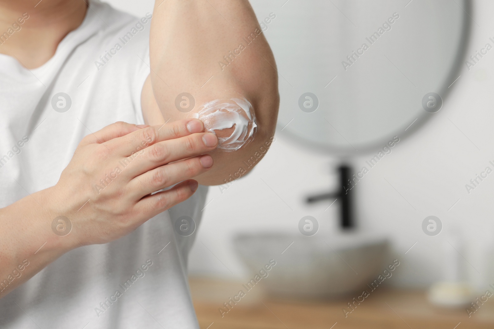 Photo of Man applying body cream onto his elbow in bathroom, closeup. Space for text