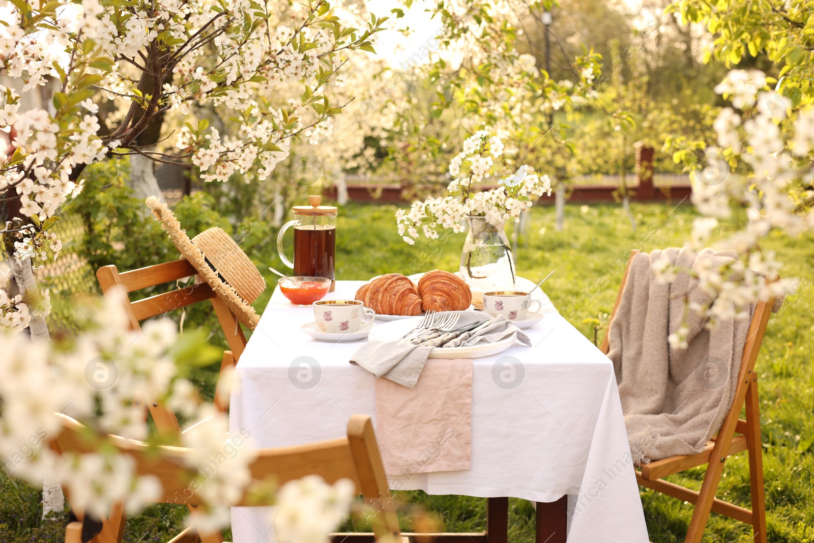 Stylish table setting with beautiful spring flowers, tea and croissants in garden Photo of Stylish table setting with beautiful spring flowers, tea and croissants in garden