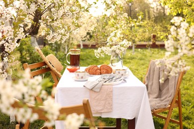 Photo of Stylish table setting with beautiful spring flowers, tea and croissants in garden