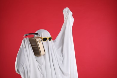 Photo of Person in ghost costume and sunglasses using retro radio receiver on red background, space for text