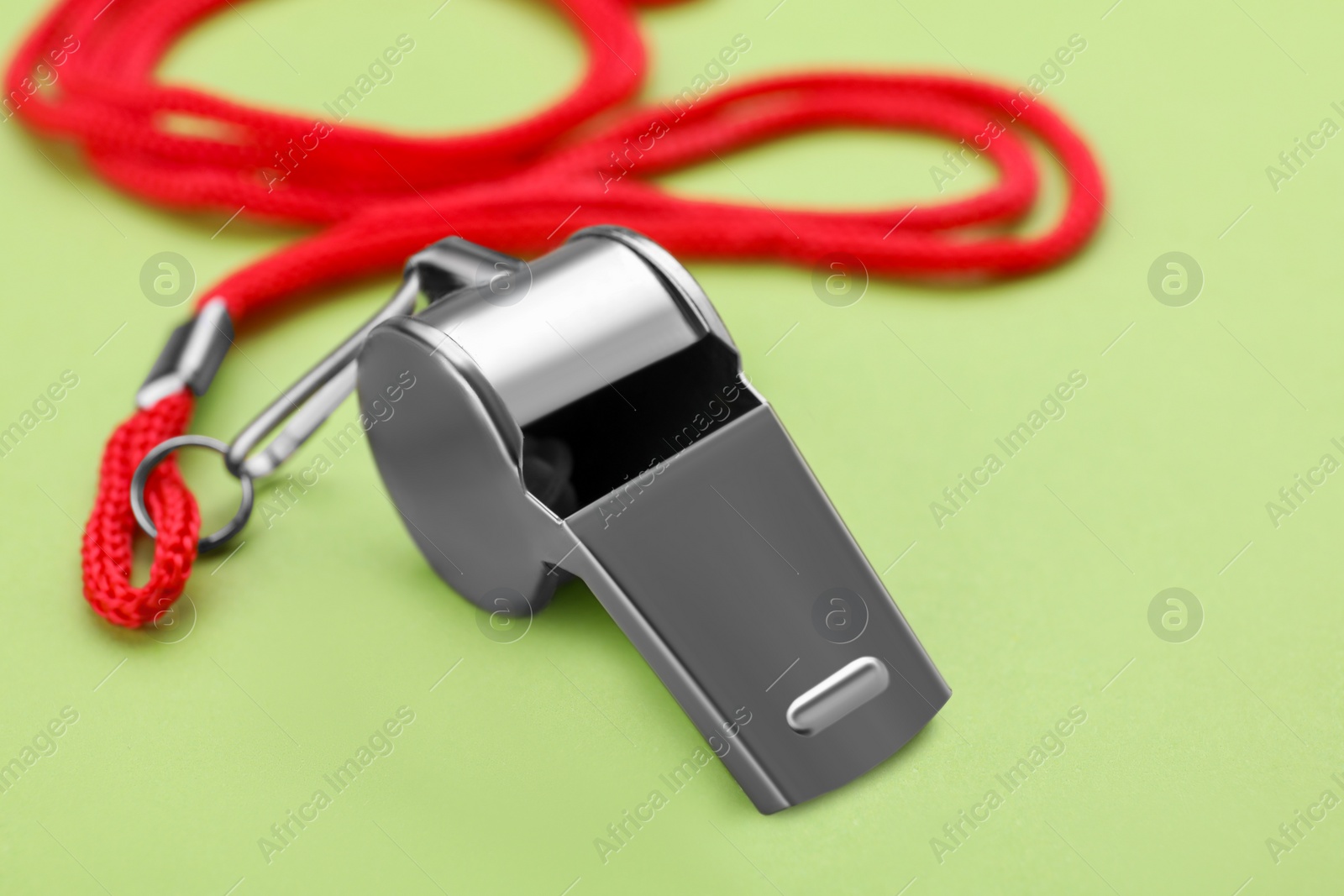 Photo of One metal whistle with red cord on light green background, closeup