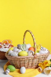 Photo of Wicker basket with festively decorated Easter eggs and beautiful tulips on white wooden table against yellow background