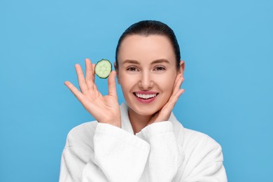 Photo of Beautiful woman with piece of cucumber on light blue background, space for text