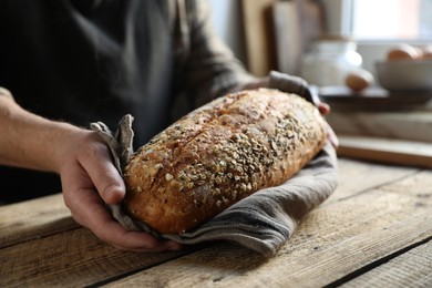 Photo of Man holding loaf of fresh bread at wooden table indoors, closeup