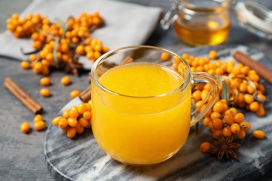 Photo of Delicious sea buckthorn tea and fresh berries on grey table, closeup