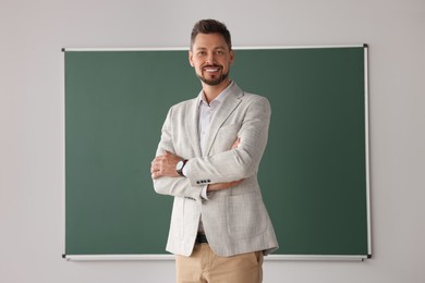 Photo of Happy teacher standing at blackboard in classroom