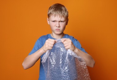 Photo of Angry boy popping bubble wrap on orange background. Stress relief