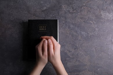 Photo of Religion. Christian woman praying over Bible at gray table, top view. Space for text