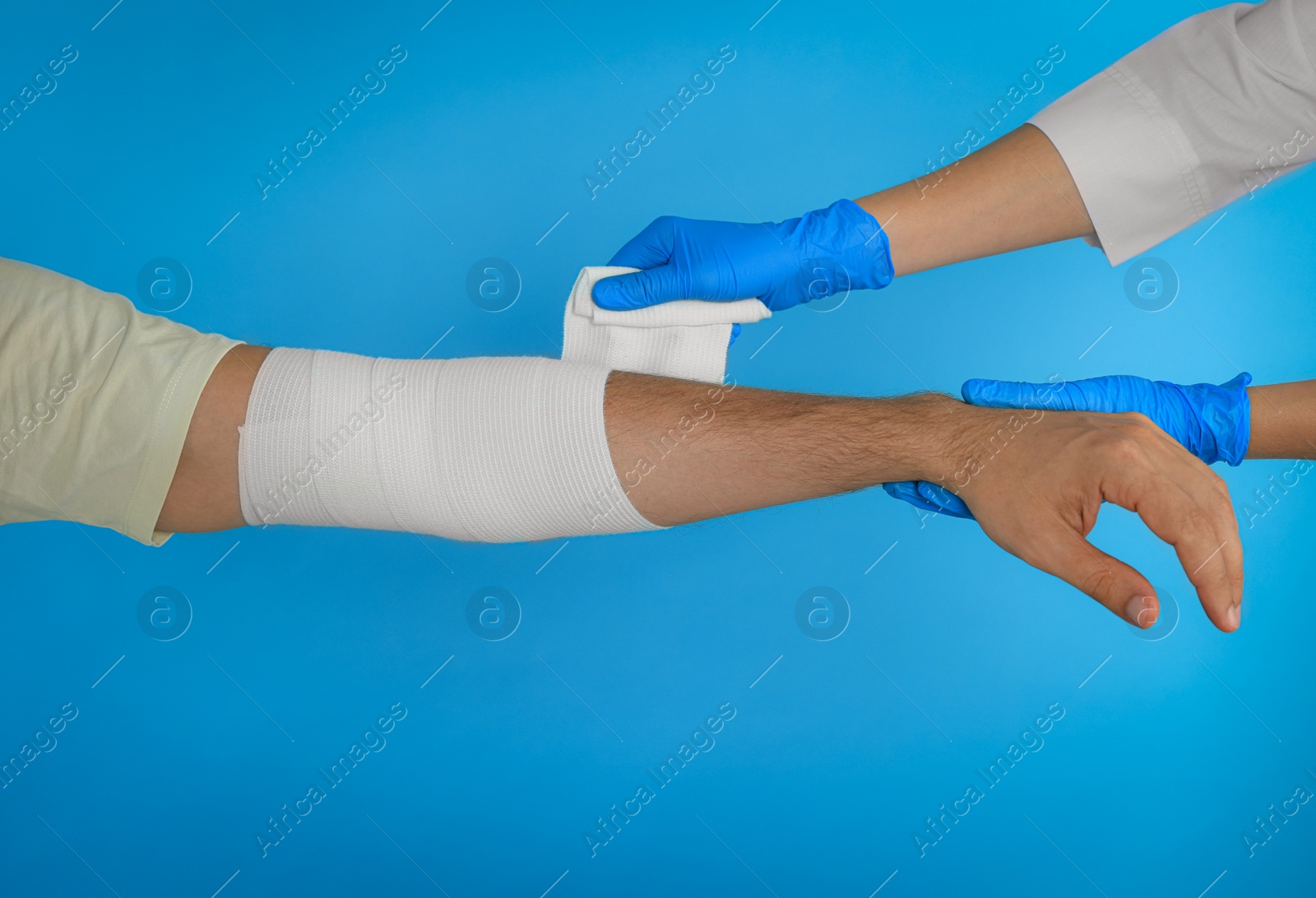 Photo of Doctor applying medical bandage onto patient's hand on light blue background, closeup