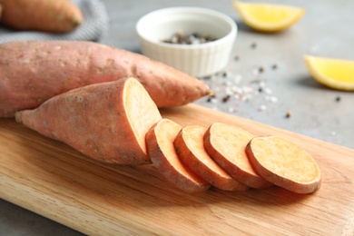 Photo of Wooden board with sweet potatoes on table, closeup