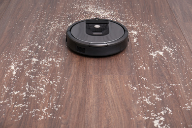 Photo of Removing groats from wooden floor with robotic vacuum cleaner at home. Space for text