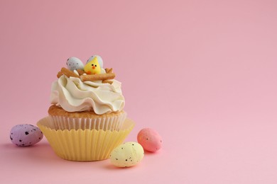 Photo of Tasty Easter cupcake with vanilla cream and candies on pink background, space for text
