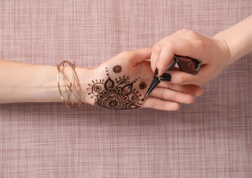 Photo of Professional mehndi master making henna tattoo at table, top view