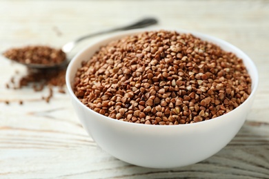 Photo of Bowl of uncooked buckwheat on white wooden table