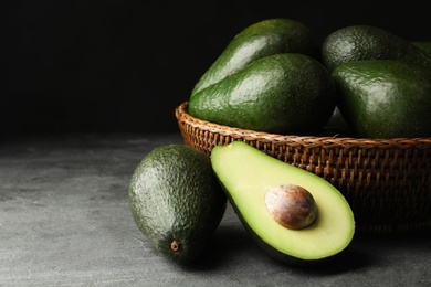 Photo of Delicious ripe avocados on grey table against dark background