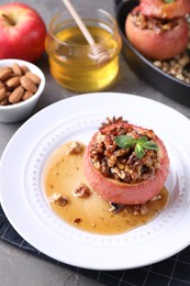 Photo of Tasty baked apple with nuts, honey and mint on gray table, closeup