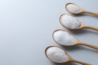 Photo of Organic white salt in spoons on light grey background. Space for text