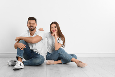 Photo of Young couple in stylish jeans sitting near white wall