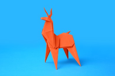 Photo of Origami art. Handmade orange paper deer on light blue background