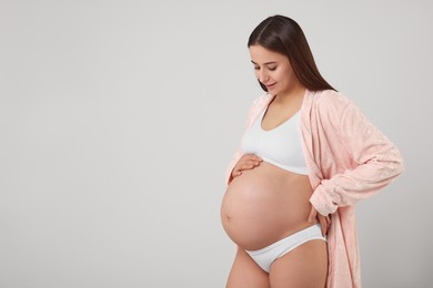 Photo of Beautiful pregnant woman in stylish comfortable underwear and robe on grey background, space for text