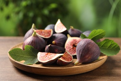 Photo of Whole and cut ripe figs with leaves on wooden table against blurred green background, closeup