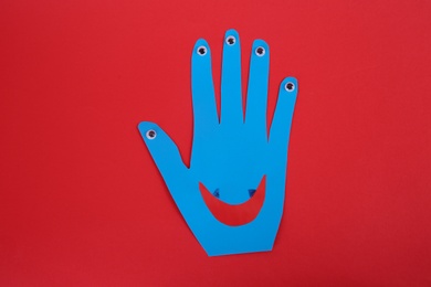 Photo of Funny blue hand shaped monster on red background, top view. Halloween decoration